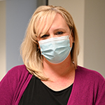 White female (Susan Bradley) long blonde hair wearing a pink cardigan and a surgical mask.